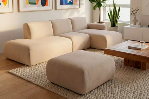 sofá chaise longue terminal, con puf, en salón decorado con cuadros, al lado de una ventana 