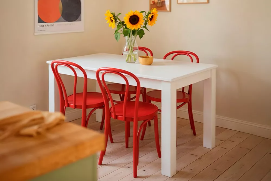 mesa de comedor extensible blanca, decorada con sillas rojas y un jarrón con flores encima