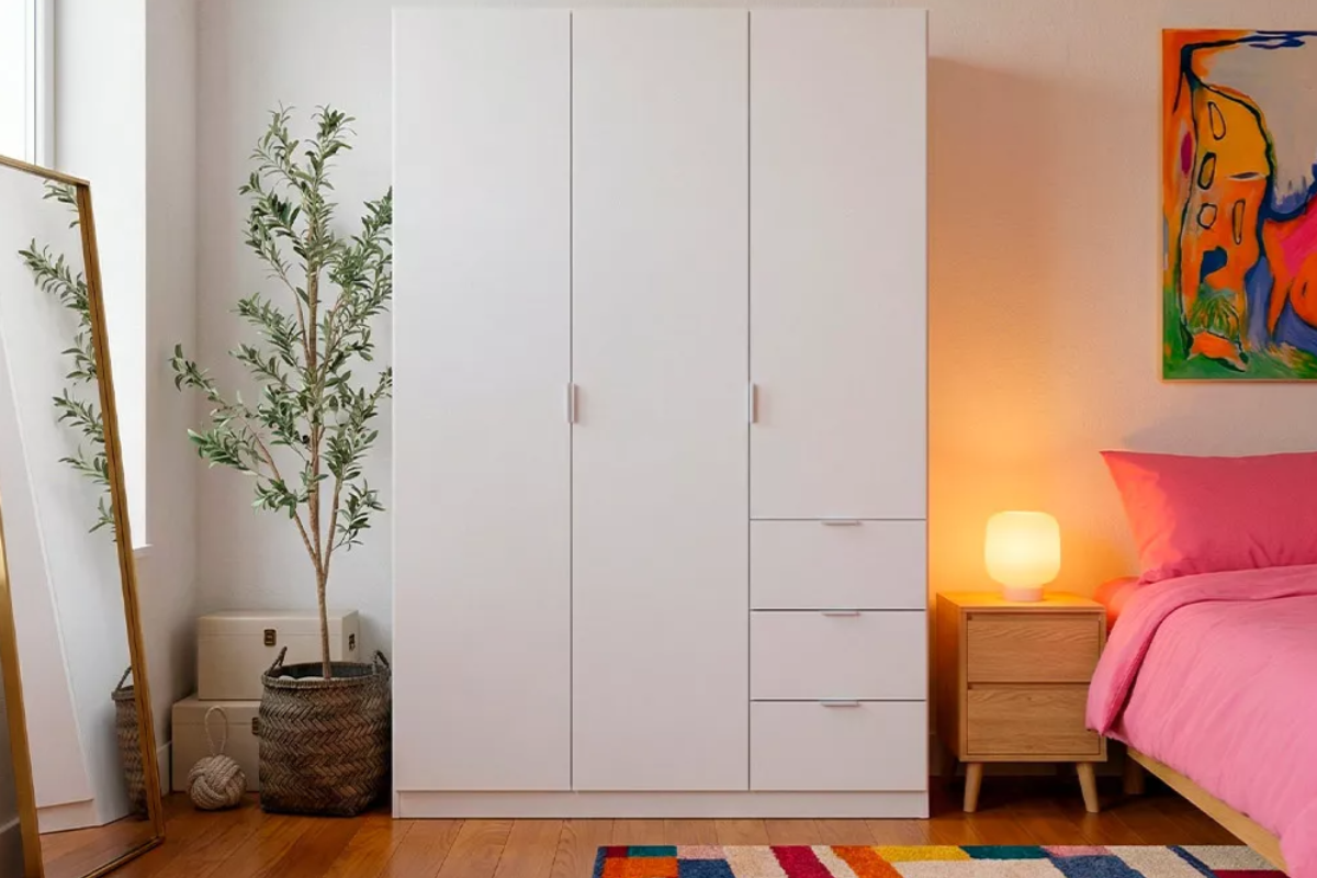 armario blanco con 3 puertas batientes y 3 cajones, colocado en una habitación decorada con un espejo y una planta artificial.