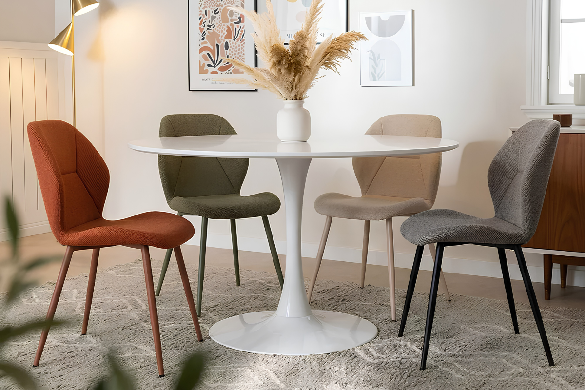 cuatro sillas comedor tapizadas de color rojo, verde, beige y gris, alrededor de una mesa de centro redonda.